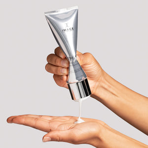 A person dispensing creamy facial cleanser from a sleek silver tube into their open palm, showcasing the MAX™ facial cleanser | IMAGE Skincare in use.