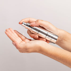 A person dispensing a clear skincare serum from a sleek silver pump bottle labeled the MAX™ serum | IMAGE Skincare into their open palm against a neutral background.