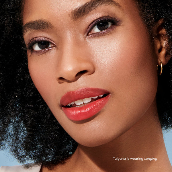 Close-up of a woman with natural curly hair wearing red lip color from Beyond Matte® Lip Stain | Jane Iredale, showcasing smooth, radiant skin and subtle eye makeup.