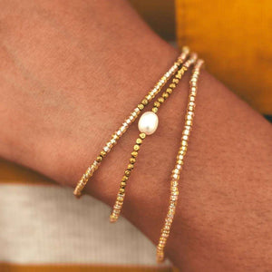 Close-up of a wrist wearing a delicate Tenere Bracelet | Purpose Jewelry featuring gold and pearl bead strands, styled with a warm-toned outfit for an elegant look.