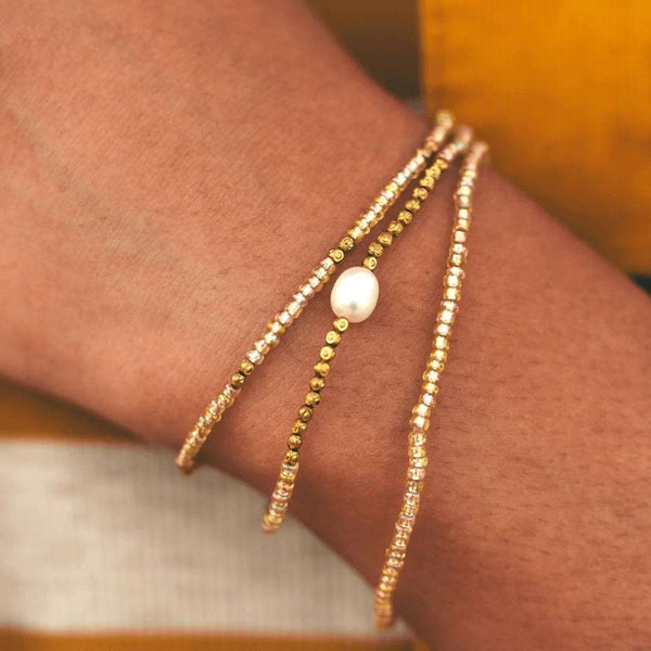 Close-up of a wrist wearing a delicate Tenere Bracelet | Purpose Jewelry featuring gold and pearl bead strands, styled with a warm-toned outfit for an elegant look.