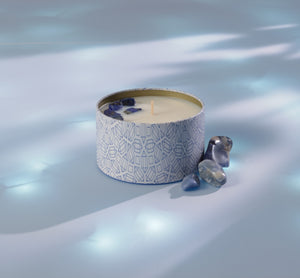 Calm Candle Tin 6 oz | Aluminate Life surrounded by smooth blue stones on a softly lit surface, evoking a serene and relaxing atmosphere.