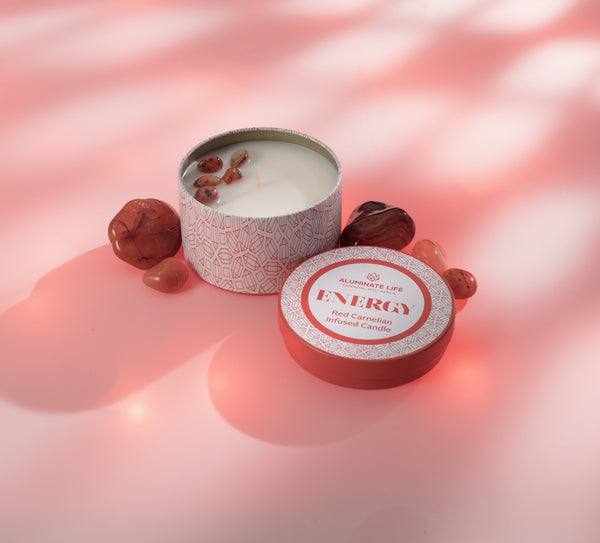 Energy Candle Tin 6 oz | Aluminate Life with red carnelian stones on a pink surface, evoking a calming wellness and spa atmosphere.