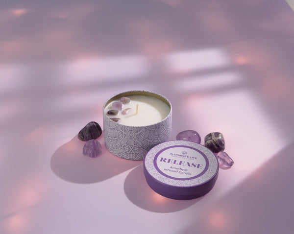 Release Candle Tin 6 oz | Aluminate Life with amethyst crystals on top, surrounded by polished amethyst stones, set on a soft pink surface with gentle natural light.