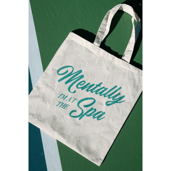 Canvas tote bag with turquoise "Mentally I'm At The Spa" script design, perfect for carrying skincare or wellness items, branded as Mentally At The Spa Tote | Lucky Owl.