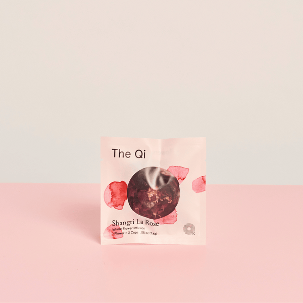 Shangri-La Rose | The Qi tea packet with rose petal design on soft pink and beige background, promoting wellness and body care through a floral infusion.