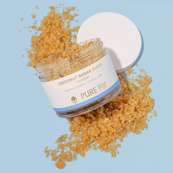 Open jar of Coconut Sugar Scrub | Pure Fiji with granulated scrub overflowing on a light blue surface, highlighting natural skincare and body care product.