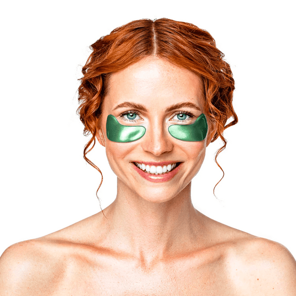 Smiling woman with red hair wearing Green Jade Eye Mask | KNESKO under her eyes, promoting skincare and wellness recovery tools.