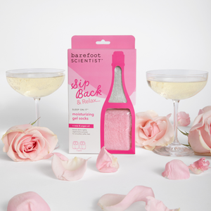 Sip Back & Relax | Barefoot Scientist moisturizing gel socks with rose and argan oil displayed with pink roses, petals, and two glasses of sparkling drink suggesting a soothing self-care moment.