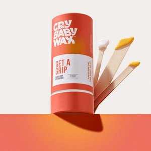 Cylindrical container of Get a Grip Face & Body Applicators | Crybaby Wax with three wooden applicators coated with skincare products, displayed against an orange and beige background.