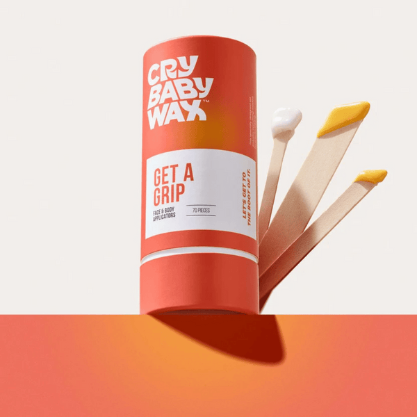 Cylindrical container of Get a Grip Face & Body Applicators | Crybaby Wax with three wooden applicators coated with skincare products, displayed against an orange and beige background.