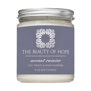 Glass jar candle labeled Mount Rainier 8oz Candle | The Beauty of Hope with lily, violet, and wild flower scent and a silver metal lid.