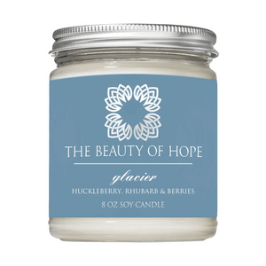 Glacier 8oz Candle | The Beauty of Hope soy candle in a clear glass jar with a silver lid, featuring a blue label with white floral logo and text describing huckleberry, rhubarb, and berries scent.