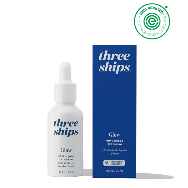 Three Ships Glow 49% Jojoba Oil Serum in white dropper bottle beside its navy blue box packaging, featuring skincare branding and EWG verified seal.