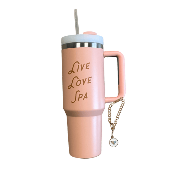 Pink insulated tumbler with handle and straw featuring gold "Live Love Spa" lettering and a small decorative charm attached, designed for wellness and hydration.