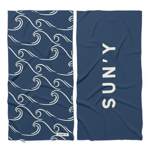 Waffle Microfiber Beach Towel - Curl | SUN'Y showing a navy blue fabric with white curling wave patterns on one side and bold SUN'Y text on the reverse, perfect for beach days.
