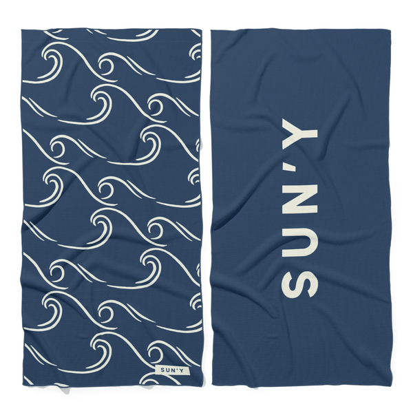 Waffle Microfiber Beach Towel - Curl | SUN'Y showing a navy blue fabric with white curling wave patterns on one side and bold SUN'Y text on the reverse, perfect for beach days.