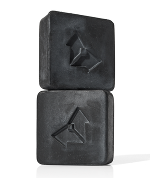 Two black square bars of Charcoal Cleansing Bar x Brisa Hennessy | Vertra stacked, featuring a subtle geometric logo embossed on each bar, highlighting skincare and wellness.