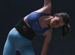 Woman wearing a Venom 2 Back | Hyperice recovery device on her lower back while stretching in athletic wear, promoting wellness and body care.