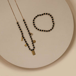 Vivid Bracelet | Purpose Jewelry featuring a delicate gold chain and black beaded design with matching bracelet, styled on a neutral beige background.