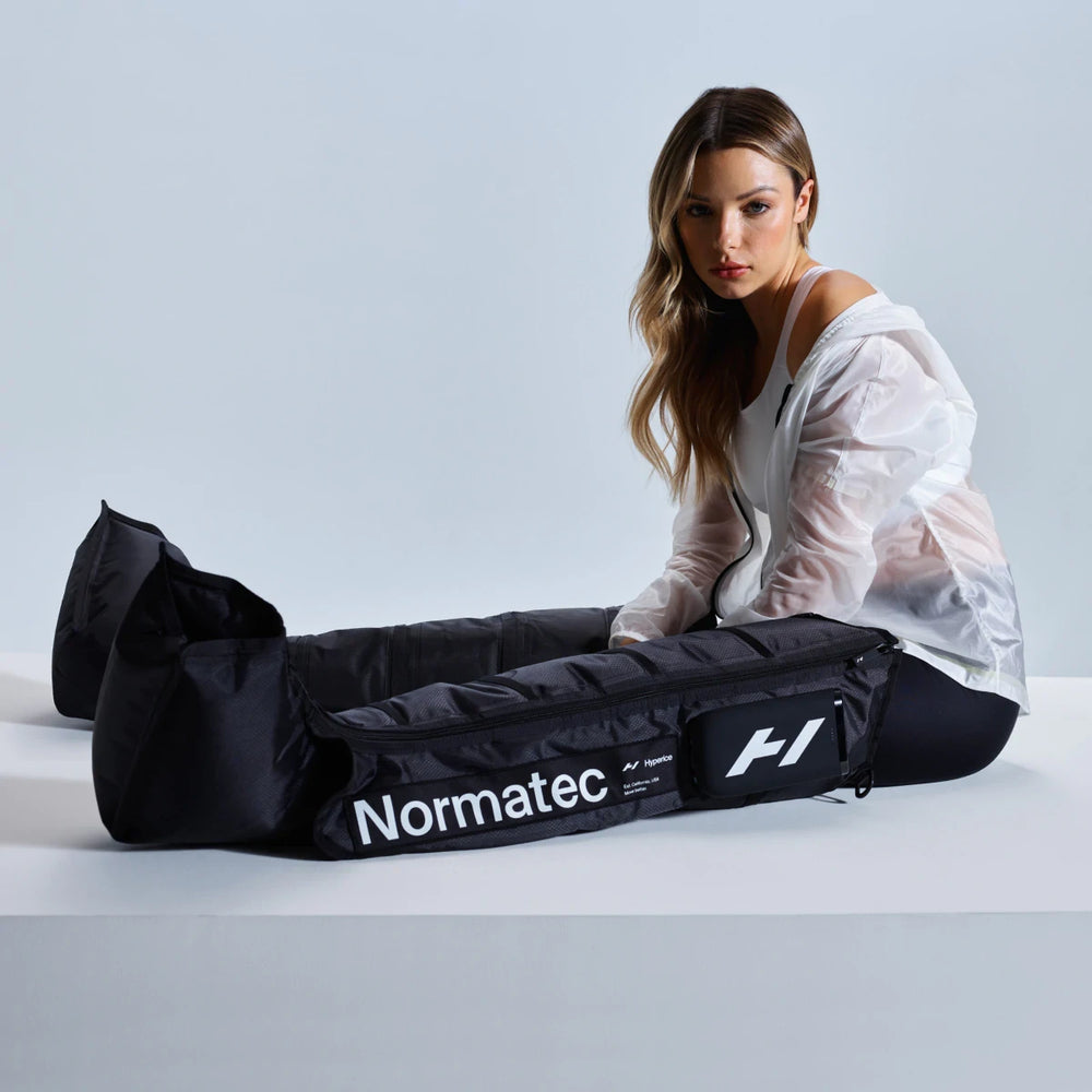 A woman wearing athletic clothing uses the Normatec Elite | Hyperice leg recovery device, designed for advanced recovery and wellness in body care and recovery tools.