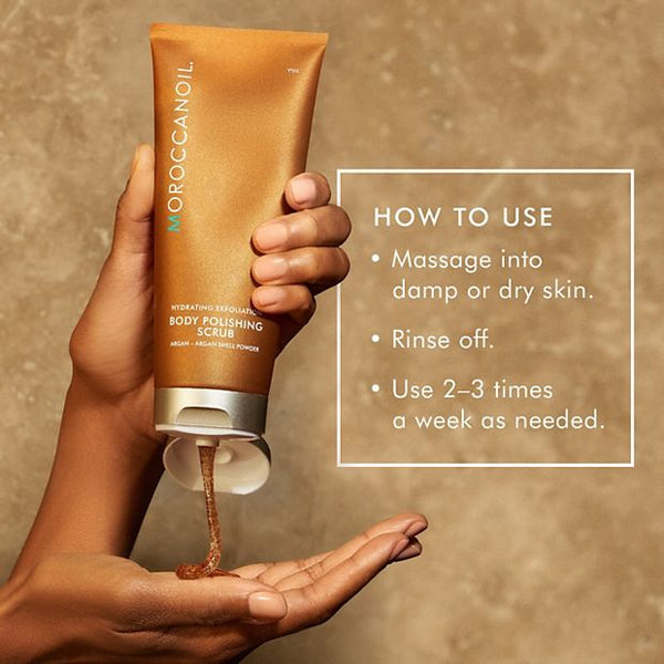 Hand holding a tube of Body Polishing Scrub | Moroccanoil dispensing brown exfoliating scrub with usage instructions for skincare and body care wellness.
