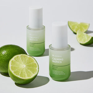 Two bottles of Calming Biotics Blemish Serum | Leaders displayed with fresh lime slices on a white background, highlighting a natural skincare product for sensitive skin.