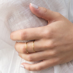 Close-up of a hand wearing two delicate gold rings on the middle finger, showcasing the Chloe Ring | Purpose Jewelry against a soft white fabric background.