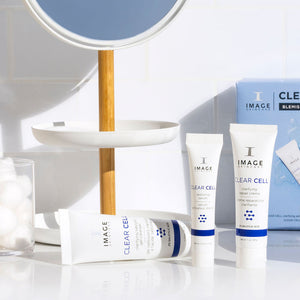 CLEAR SKIN SOLUTIONS Blemish Defense Trio | IMAGE Skincare set displayed on a white countertop with a mirror and cotton balls in the background, highlighting skincare products for blemish defense.