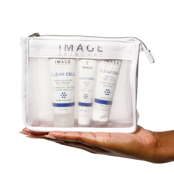 CLEAR SKIN SOLUTIONS Blemish Defense Trio | IMAGE Skincare displayed in a transparent white zippered pouch held in a hand, featuring skincare products for blemish defense.