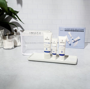 CLEAR SKIN SOLUTIONS Blemish Defense Trio | IMAGE Skincare displayed with three skincare tubes on a white tray, a clear cosmetic bag, and the product box in a bright, clean setting.