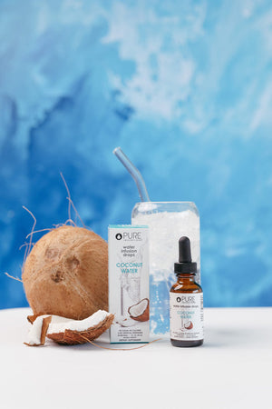 Coconut Water Infusion Drops | Pure Inventions bottle and packaging displayed next to fresh coconut pieces and a glass of iced water with a straw on a white surface with a blue background.