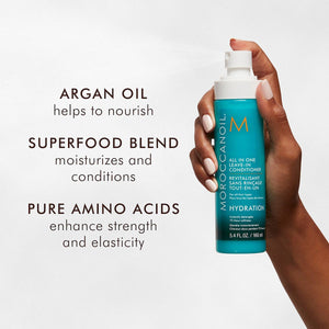 Hand holding a bottle of All in One Leave-In Conditioner - Travel | Moroccanoil with text highlighting argan oil nourishing, superfood blend moisturizing and conditioning, and pure amino acids enhancing strength and elasticity.