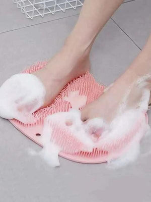 Feet being cleaned and exfoliated with foam on a pink silicone Back & Foot Scrubber | Dreambox Beauty placed on a bathroom floor.