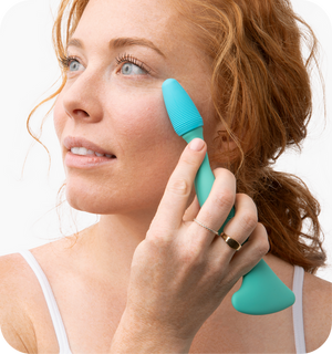 Woman with red hair using a turquoise Face Roller | RAD on her cheek, demonstrating a skincare tool designed for facial massage and wellness.