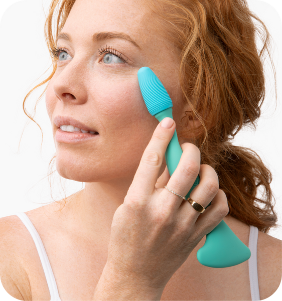 Woman with red hair using a turquoise Face Roller | RAD on her cheek, demonstrating a skincare tool designed for facial massage and wellness.