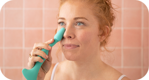 Woman using a teal Face Roller | RAD on her face against a soft pink tiled background, promoting skincare and wellness.