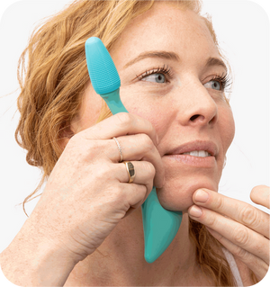 Woman using a turquoise silicone facial cleansing tool on her cheek, demonstrating skincare routine with the Face Roller | RAD for gentle facial massage and wellness.