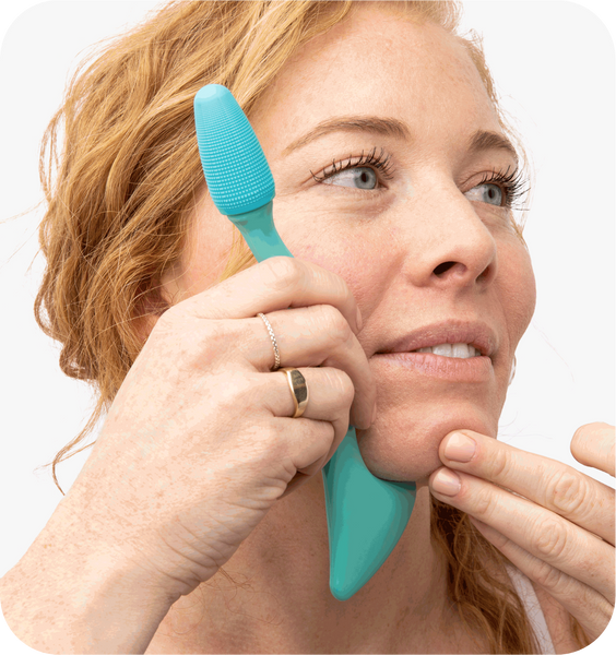 Woman using a turquoise silicone facial cleansing tool on her cheek, demonstrating skincare routine with the Face Roller | RAD for gentle facial massage and wellness.