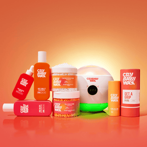 Various Crybaby Wax skincare and body care products displayed on an orange surface with a warm glowing background, featuring Get a Grip Face & Body Applicators | Crybaby Wax.