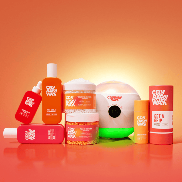 Various Crybaby Wax skincare and body care products displayed on an orange surface with a warm glowing background, featuring Get a Grip Face & Body Applicators | Crybaby Wax.