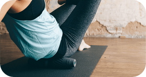Person using a black RAD HELIX | RAD foam roller on a yoga mat for recovery and muscle relief in a wellness setting.
