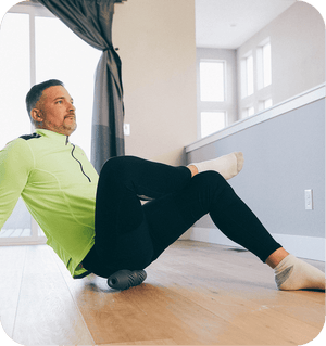 A man in athletic wear uses the RAD HELIX | RAD recovery tool for muscle relief while seated on a wooden floor in a bright, modern room.