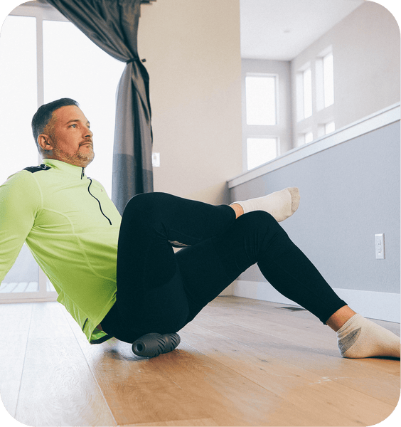 A man in athletic wear uses the RAD HELIX | RAD recovery tool for muscle relief while seated on a wooden floor in a bright, modern room.