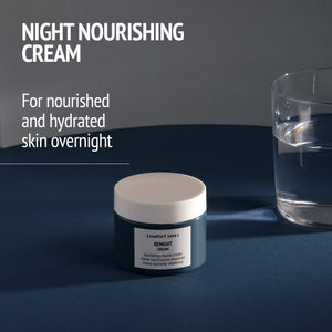 Jar of Kit Night Garden | [ comfort zone ] nourishing night cream on a dark surface next to a glass of water with soft lighting, promoting hydration and skin nourishment overnight