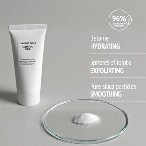 Tube of Essential Scrub | [ comfort zone ] with text highlighting hydrating betaine, exfoliating jojoba spheres, and smoothing pure silica particles, accompanied by a small glass dish with white scrub particles.