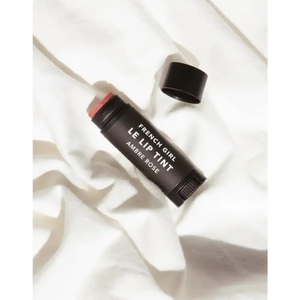 Le Lip Tint | French Girl in a sleek black tube with a soft warm rose tint, displayed on a textured white fabric background for a natural skincare look.