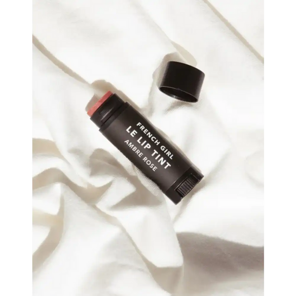 Le Lip Tint | French Girl in a sleek black tube with a soft warm rose tint, displayed on a textured white fabric background for a natural skincare look.