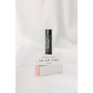 Le Lip Tint | French Girl in black tube packaging standing on a white and light pink box with minimalist design on a soft white background.