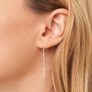 Close-up of a woman's ear wearing delicate silver Love Light Earrings | Little Sparkles with a slender textured bar design against a light background.